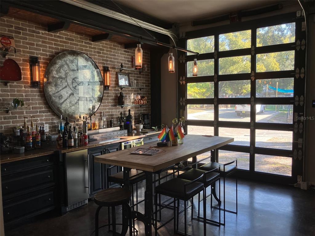 A home bar with brick walls, a large round mirror, and a glass garage door — 6401 N NEBRASKA AVENUE, TAMPA, FL