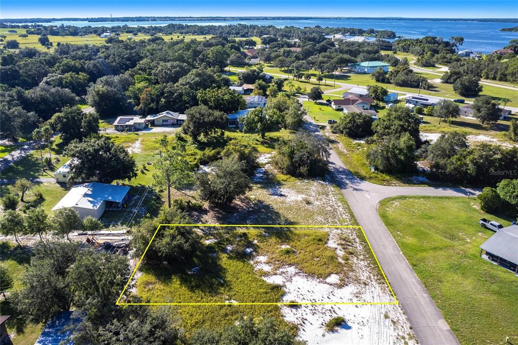 An aerial view shows a vacant, rectangular lot outlined in yellow next to a paved road — 917 HOLLYHOCK COURT, LAKE PLACID, FL