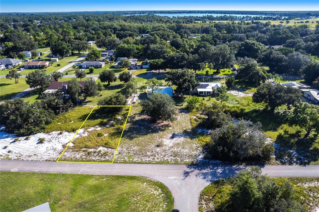 An aerial view shows a vacant, rectangular lot outlined in yellow along a paved road — 917 HOLLYHOCK COURT, LAKE PLACID, FL
