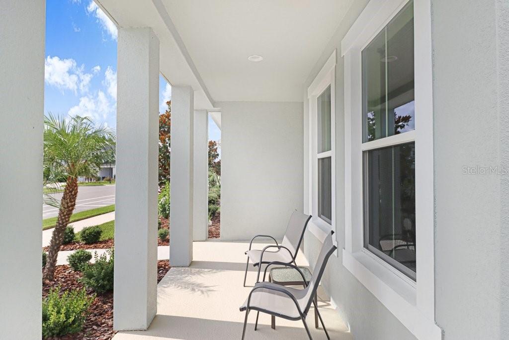 A covered front porch features light-colored walls, square columns, and two outdoor chairs — 3847 LAJUANA BOULEVARD, WESLEY CHAPEL, FL