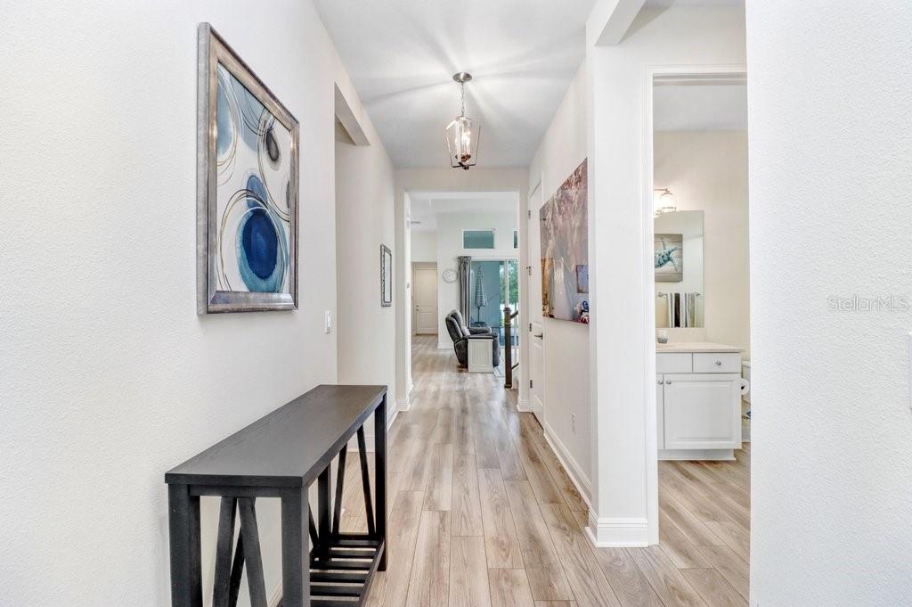 A hallway with light wood-look flooring, a dark console table, and a view into a bathroom — 3847 LAJUANA BOULEVARD, WESLEY CHAPEL, FL