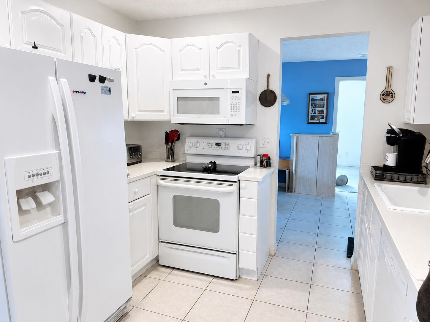 A white kitchen features a refrigerator, stove, microwave, and tile flooring — 14582 Sunny Waters Lane, Delray Beach FL 33484, DELRAY BEACH, FL