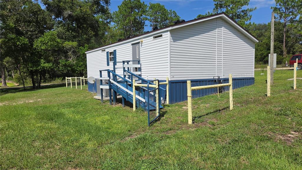 The exterior of a white mobile home features a blue staircase and a wire fence — 1298 NE BOROS DRIVE, WILLISTON, FL
