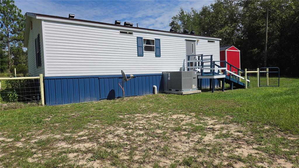 A white mobile home with blue skirting, a small wooden deck, and a red shed — 1298 NE BOROS DRIVE, WILLISTON, FL