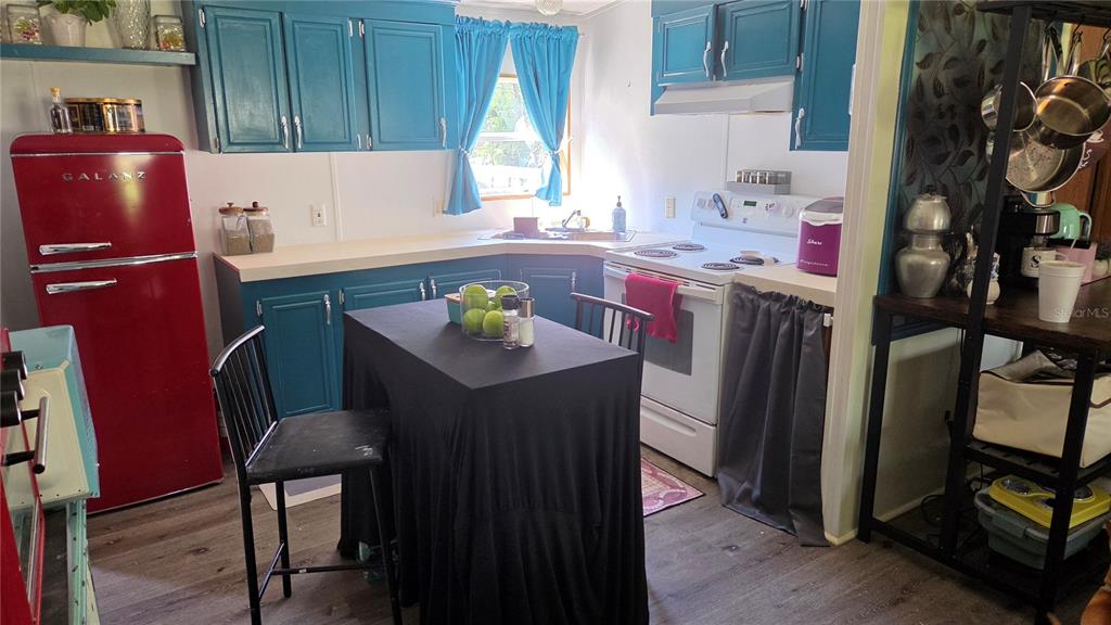 A kitchen features blue cabinets, a red refrigerator, a black-covered table, and white appliances — 1298 NE BOROS DRIVE, WILLISTON, FL