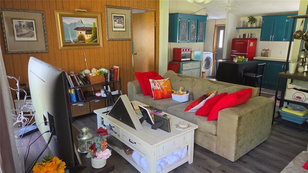 A living room with wood-paneled walls, a tan sofa, and an open kitchen with teal cabinets — 1298 NE BOROS DRIVE, WILLISTON, FL