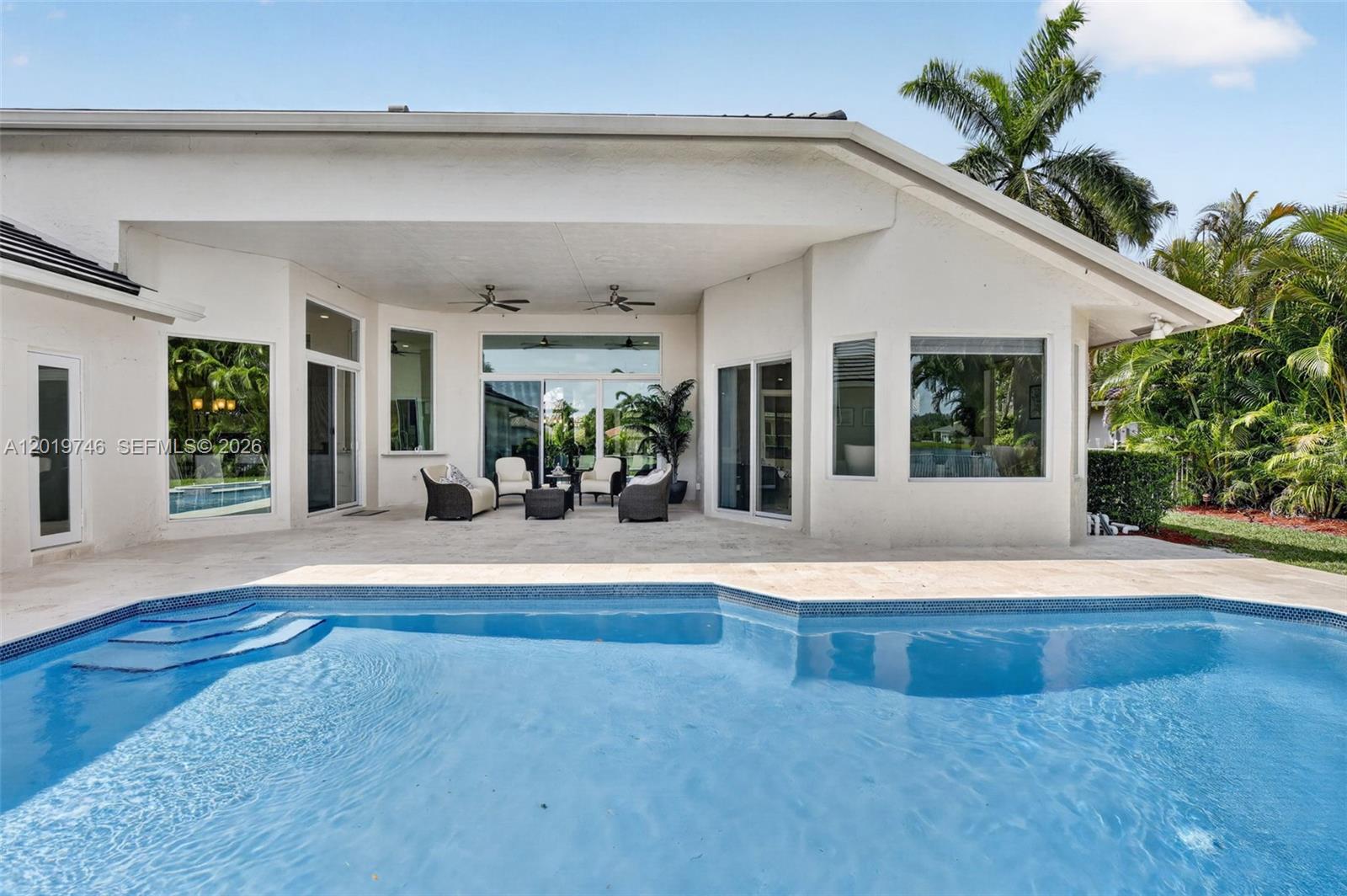 A swimming pool sits in front of a covered patio with outdoor furniture and windows — 2922 Medinah, Weston FL 33332, WESTON, FL