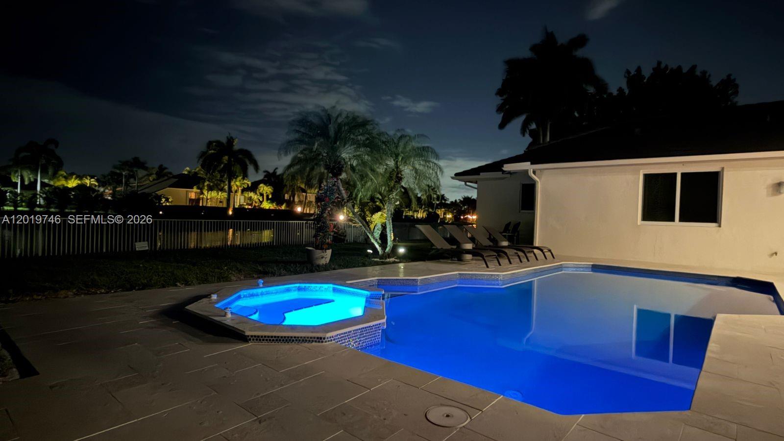 A backyard swimming pool and attached spa are illuminated at night beside a house — 2922 Medinah, Weston FL 33332, WESTON, FL