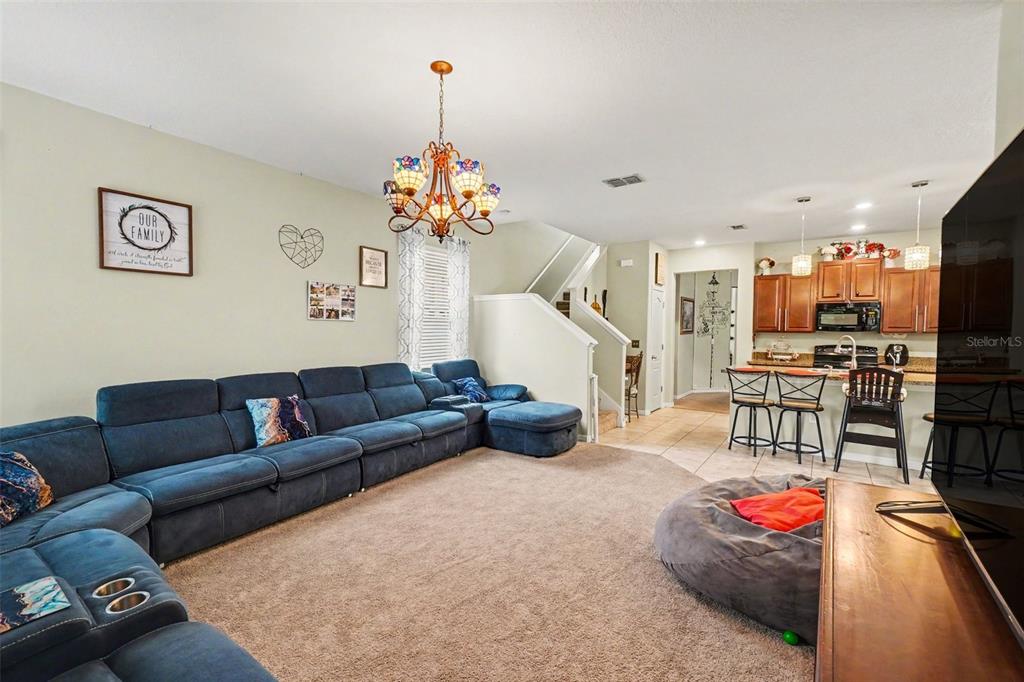 A living room with a large blue sectional sofa, beige carpet, and an open kitchen — 11334 VILLAS ON THE GREEN DR, RIVERVIEW, FL