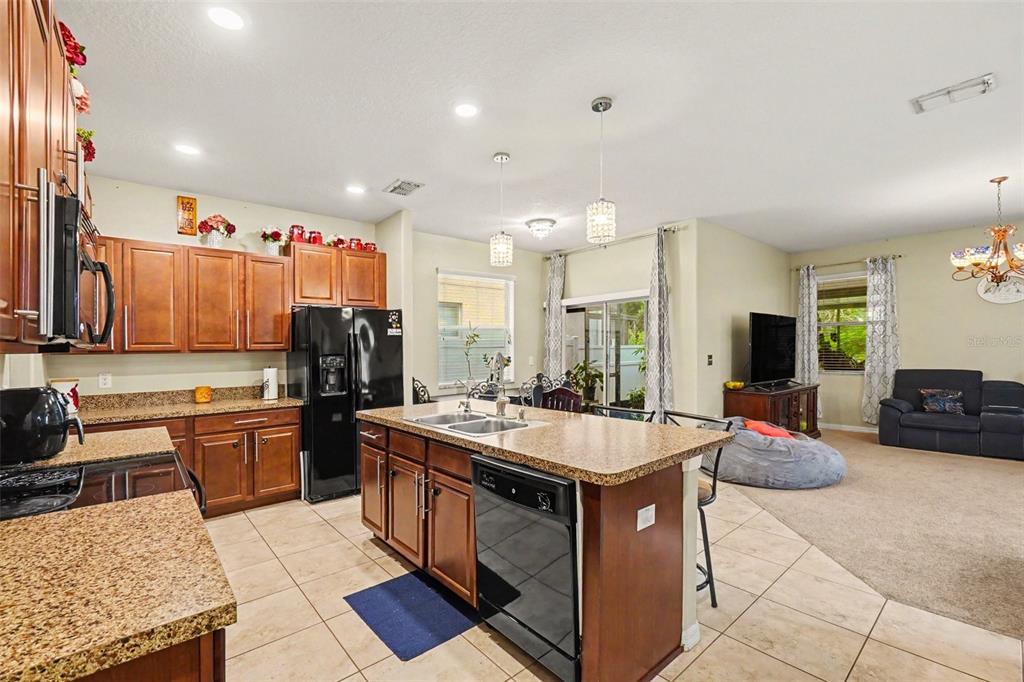 A kitchen with wood cabinets, granite countertops, and a center island opens to a living area — 11334 VILLAS ON THE GREEN DR, RIVERVIEW, FL