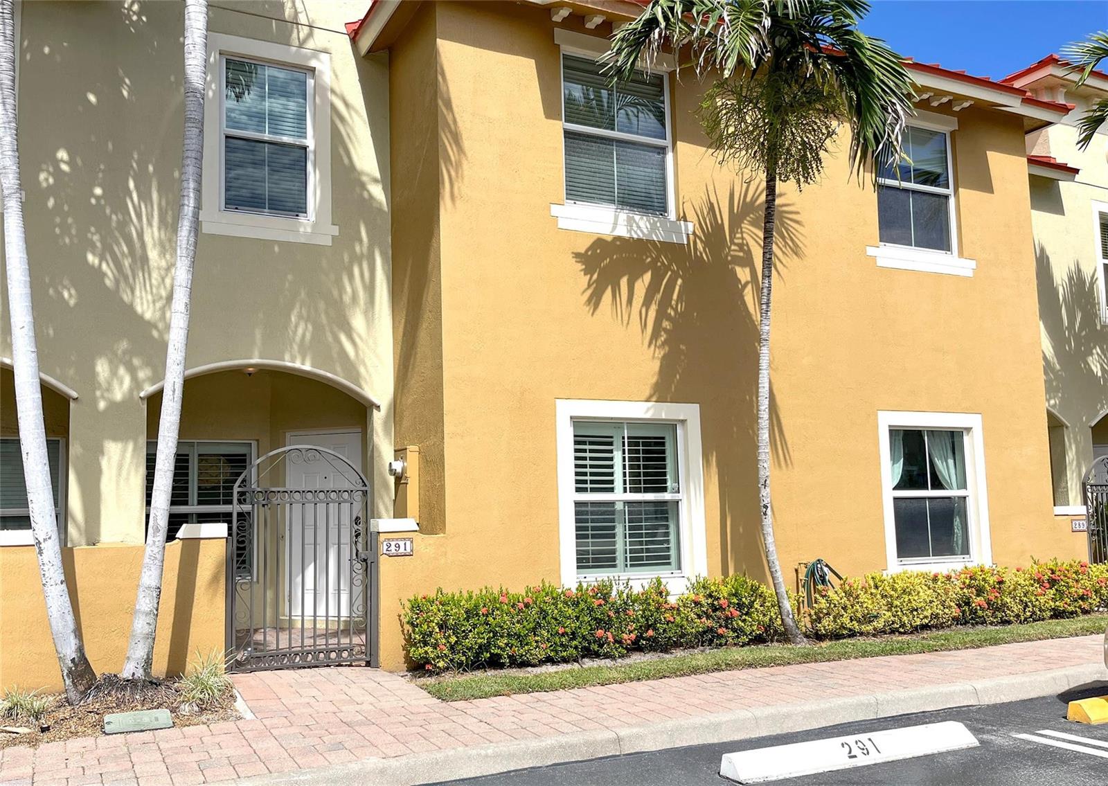 A two-story yellow stucco townhouse features a gated entryway, palm trees, and a parking space — 291 Lake Monterey Circle, Boynton Beach FL 33426, BOYNTON BEACH, FL