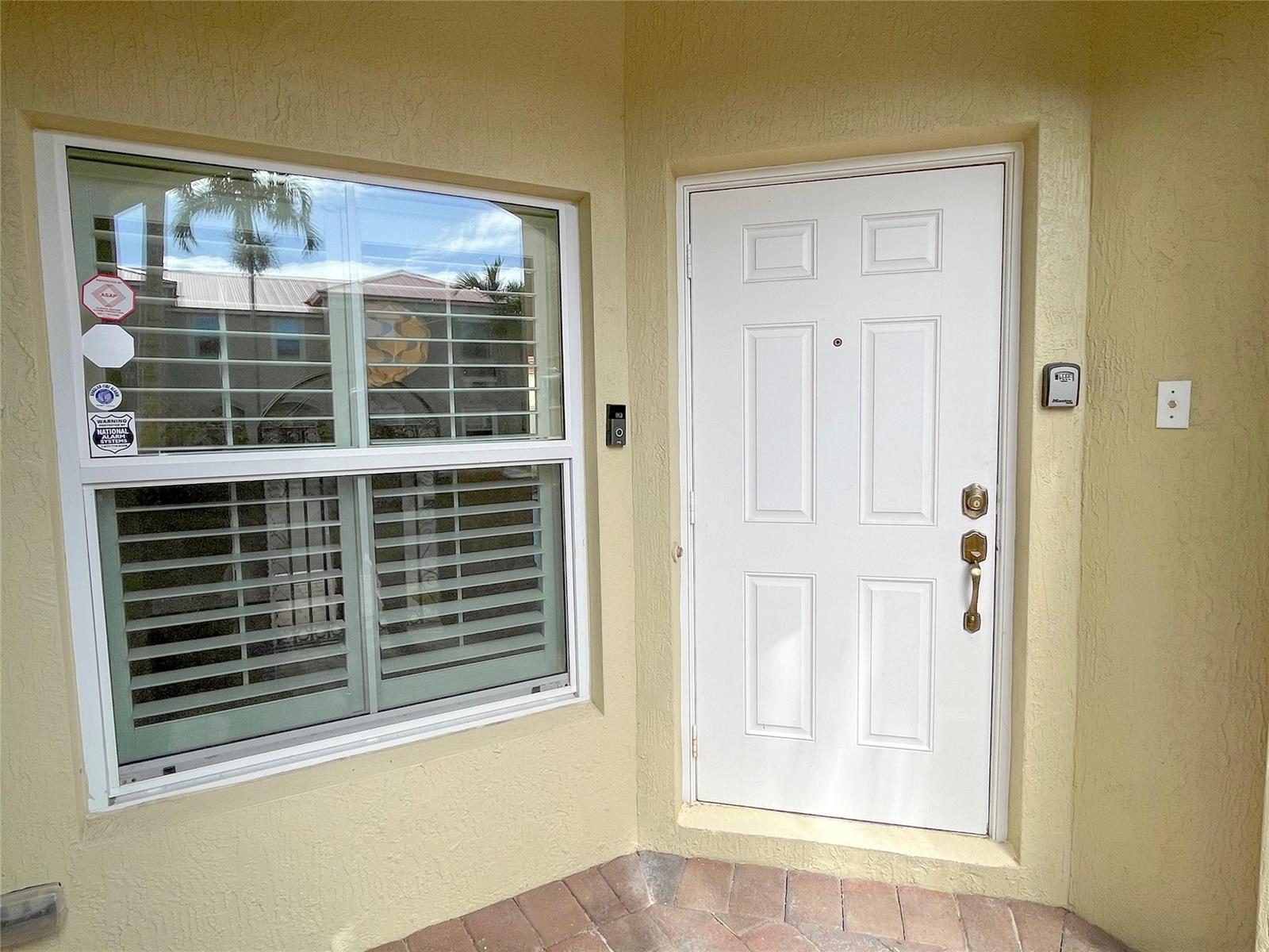 A white front door and a window with shutters are set in a yellow wall — 291 Lake Monterey Circle, Boynton Beach FL 33426, BOYNTON BEACH, FL