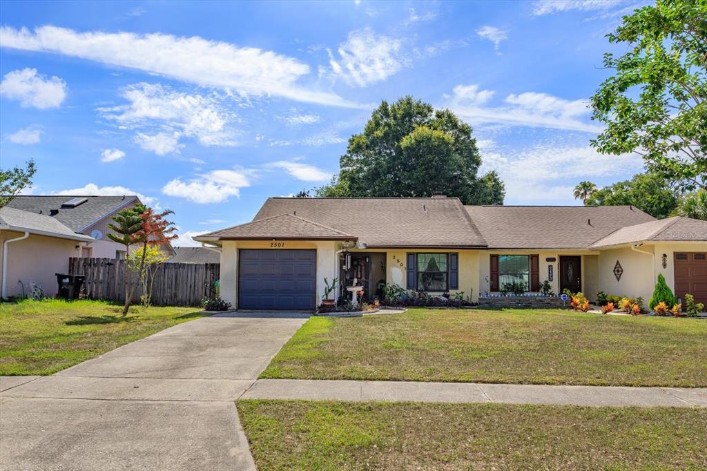A single-story house with a beige exterior, a dark garage door, and a grassy front yard — 2501 LONG MEADOW WAY, ORLANDO, FL