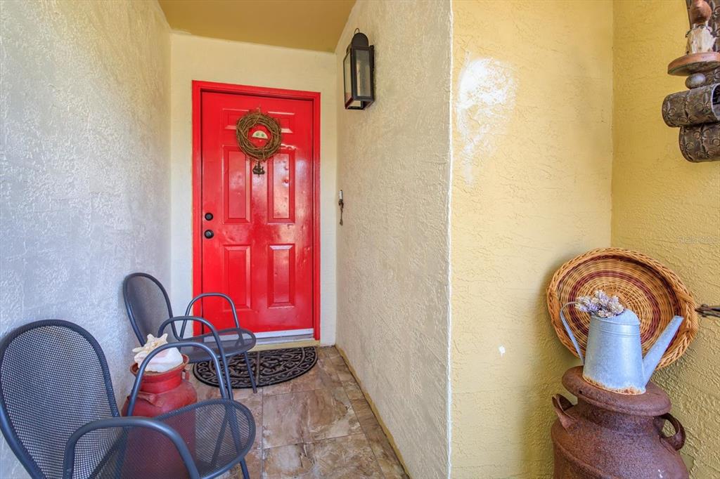 A bright red front door sits on a tiled porch with metal chairs and decor — 2501 LONG MEADOW WAY, ORLANDO, FL