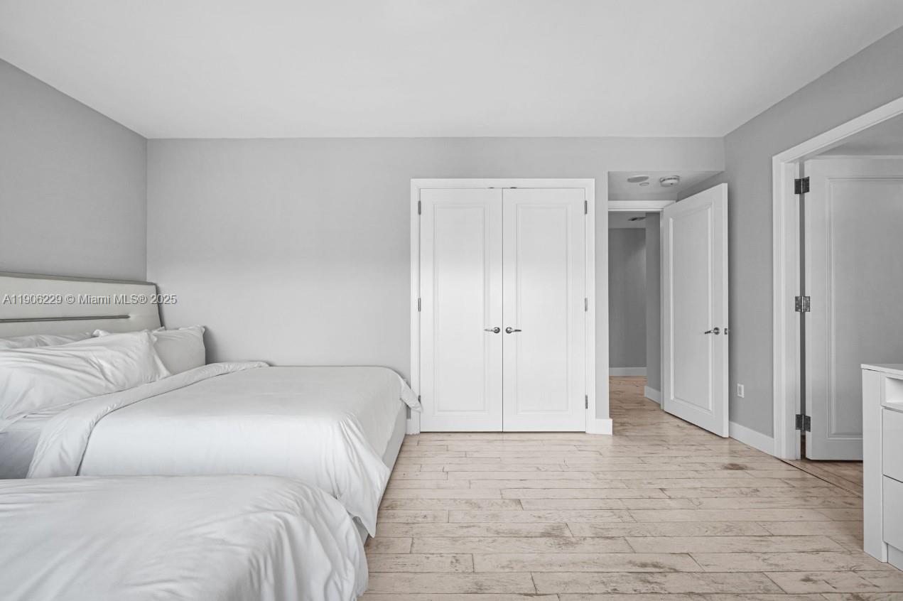 A bedroom features light wood-look flooring, white walls, a bed, and white double closet doors — 1435 Brickell Ave # 3401, Miami FL 33131, MIAMI, FL