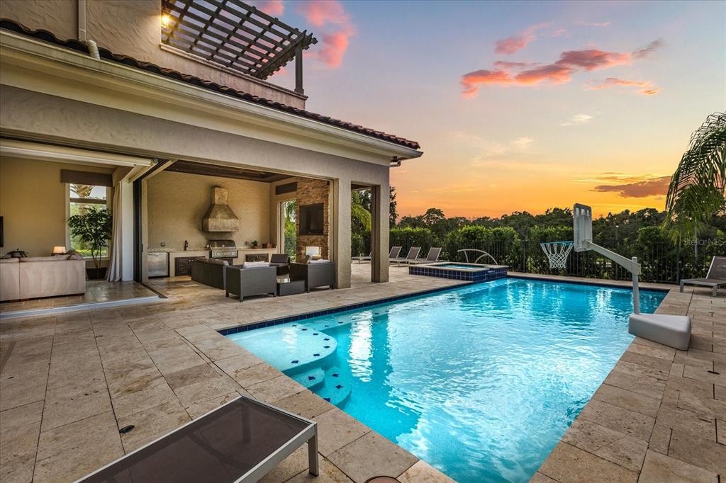 A covered patio with an outdoor kitchen overlooks a swimming pool at sunset — 7863 PALMILLA COURT, REUNION, FL