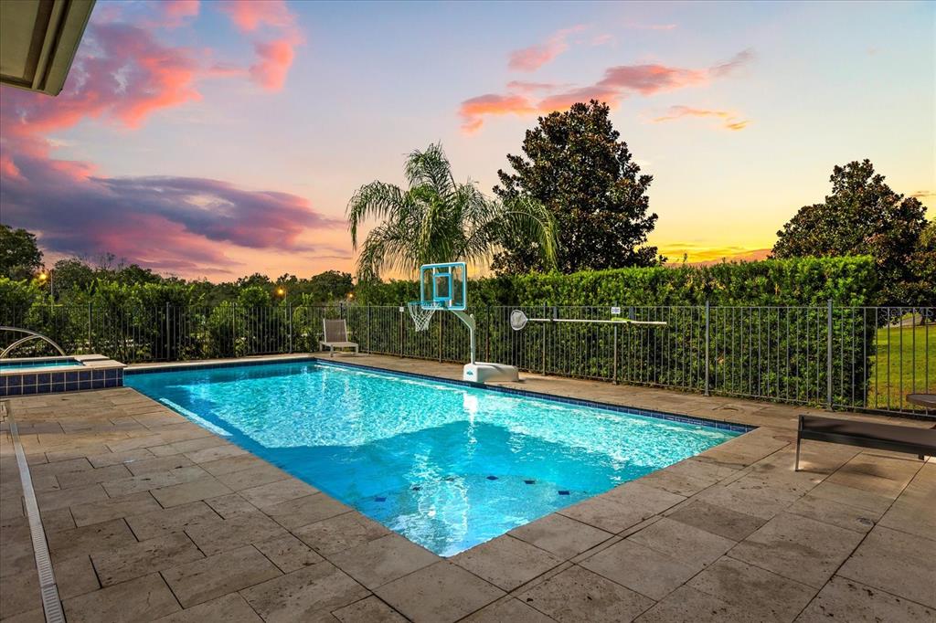 A rectangular swimming pool with a basketball hoop sits on a stone patio at sunset — 7863 PALMILLA COURT, REUNION, FL