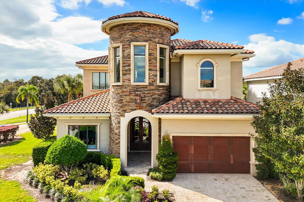 A two-story house with a stone-clad turret, arched entryway, and a brown garage door — 7863 PALMILLA COURT, REUNION, FL