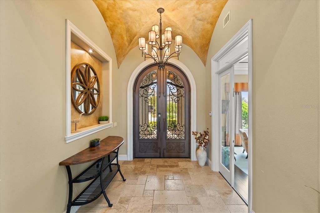 An entryway features a barrel-vaulted ceiling, a chandelier, a console table, and double iron doors — 7863 PALMILLA COURT, REUNION, FL