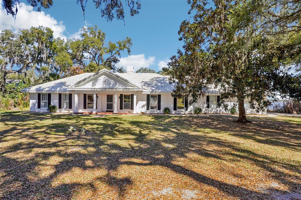 A single-story white house with a gabled roof sits on a large, tree-shaded lawn — 37048 COUNTY ROAD 452, GRAND ISLAND, FL