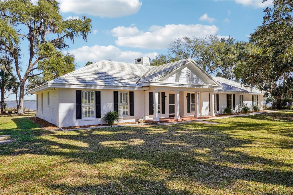 A white, single-story ranch-style house with a tiled roof sits on a grassy, tree-filled lot — 37048 COUNTY ROAD 452, GRAND ISLAND, FL