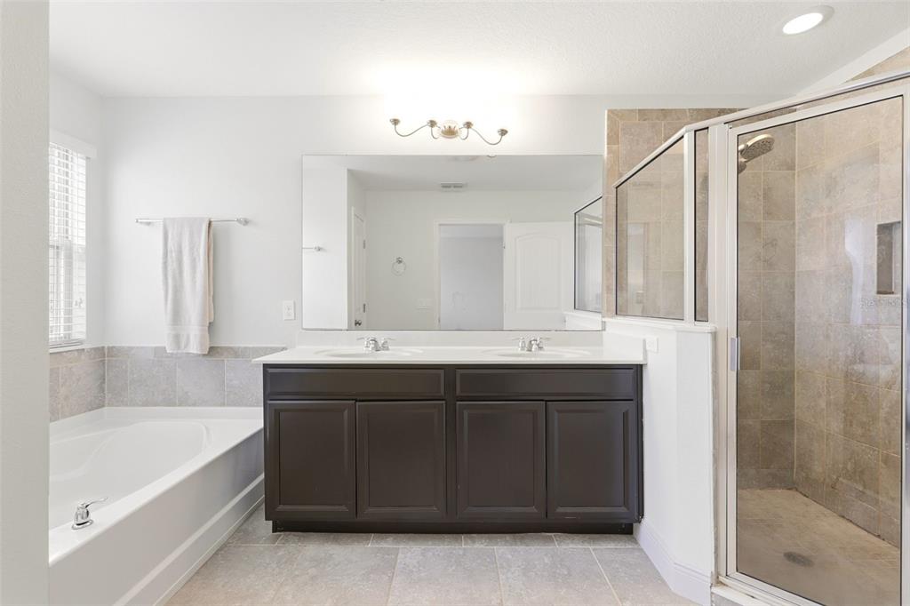 A bathroom features a double vanity with dark cabinets, a soaking tub, and a glass shower — 10558 GREEN IVY LANE, ORLANDO, FL