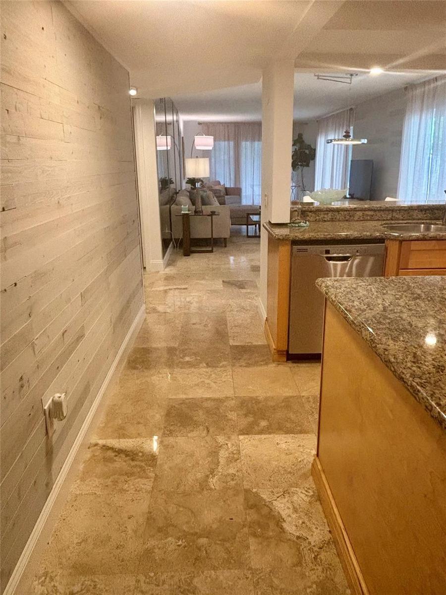 A hallway with light wood-plank walls leads past a kitchen toward a living room area — 10980 S Ocean Drive # 114, Jensen Beach FL 34957, JENSEN BEACH, FL