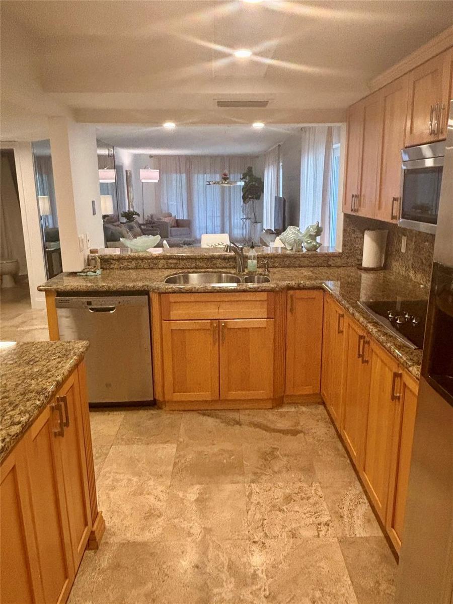A kitchen with light wood cabinets, granite countertops, stainless steel appliances, and stone flooring — 10980 S Ocean Drive # 114, Jensen Beach FL 34957, JENSEN BEACH, FL