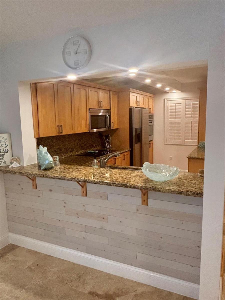 A kitchen with wood cabinets, granite countertops, and a shiplap-paneled breakfast bar — 10980 S Ocean Drive # 114, Jensen Beach FL 34957, JENSEN BEACH, FL