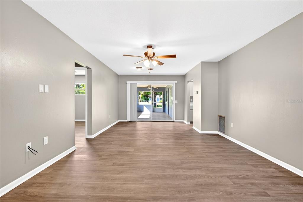 An empty living room features light gray walls, wood-look flooring, and a sliding glass door — 3423 SW 27TH STREET, OCALA, FL
