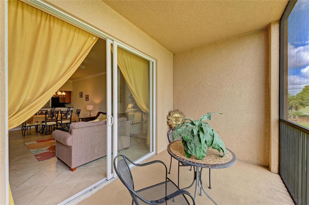 A covered balcony with a small bistro table and chairs overlooks a view through screens — 8309 GRAND ESTUARY TRAIL UNIT 205, BRADENTON, FL