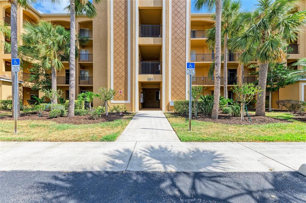 A multi-story apartment building exterior features a central walkway, palm trees, and two handicap signs — 8309 GRAND ESTUARY TRAIL UNIT 205, BRADENTON, FL