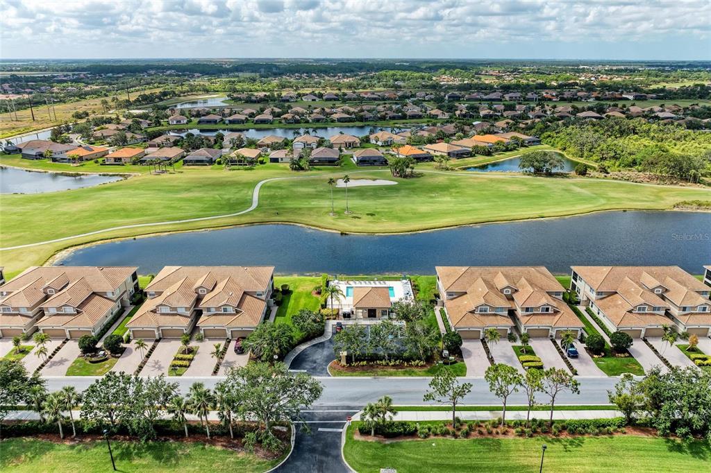 An aerial view shows townhomes with a community pool overlooking a golf course and lake — 8309 GRAND ESTUARY TRAIL UNIT 205, BRADENTON, FL