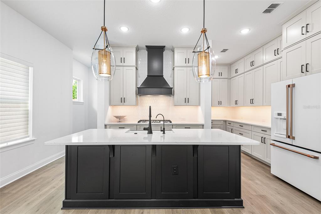 A modern kitchen features a black island, white cabinetry, a dark range hood, and pendant lights — 1619 S OSCEOLA AVENUE, ORLANDO, FL