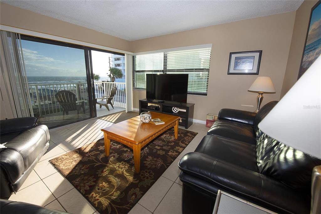 A living room with black leather sofas, a wooden coffee table, and a balcony view — 1571 S ATLANTIC AVENUE UNIT 303, NEW SMYRNA BEACH, FL