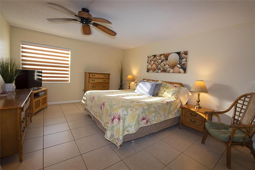 A bedroom features a king bed, tile flooring, a ceiling fan, and wooden furniture — 1571 S ATLANTIC AVENUE UNIT 303, NEW SMYRNA BEACH, FL