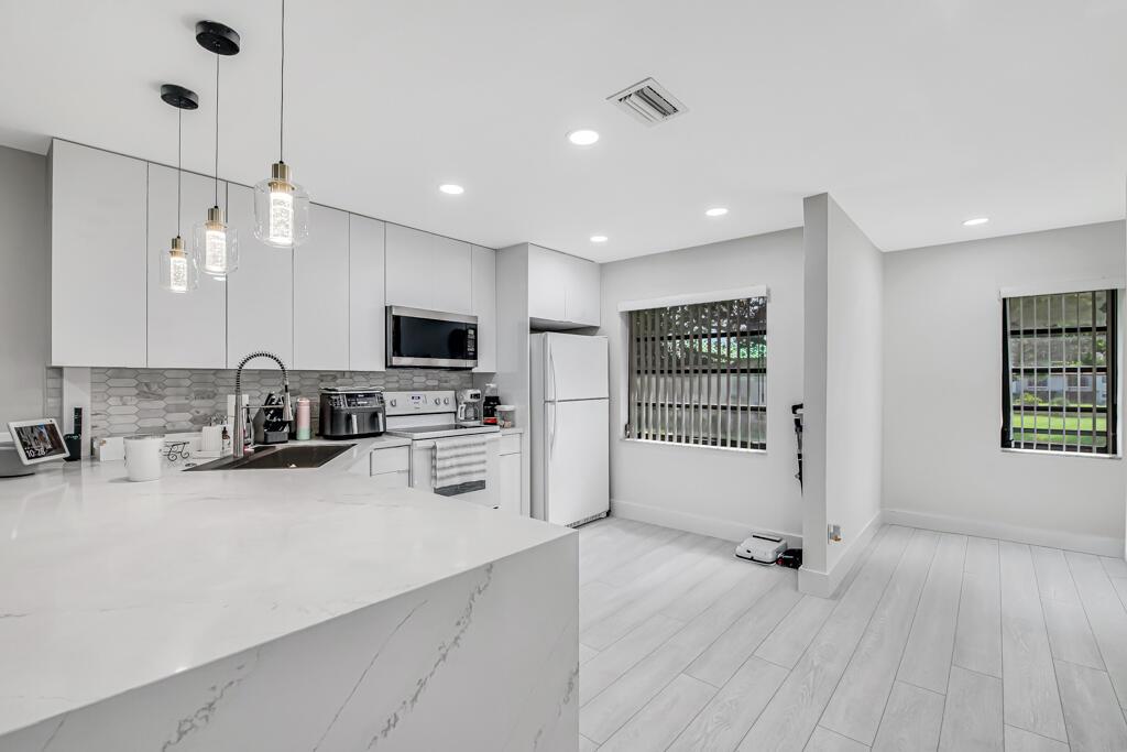 A modern kitchen features white cabinetry, marble-look countertops, stainless steel appliances, and light wood flooring — 21362 Juego Circle # D, Boca Raton FL 33433, BOCA RATON, FL