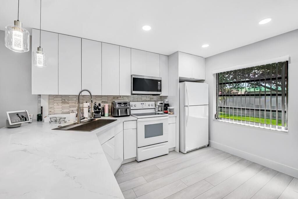 A modern kitchen features white cabinetry, quartz countertops, a white stove, and a white refrigerator — 21362 Juego Circle # D, Boca Raton FL 33433, BOCA RATON, FL