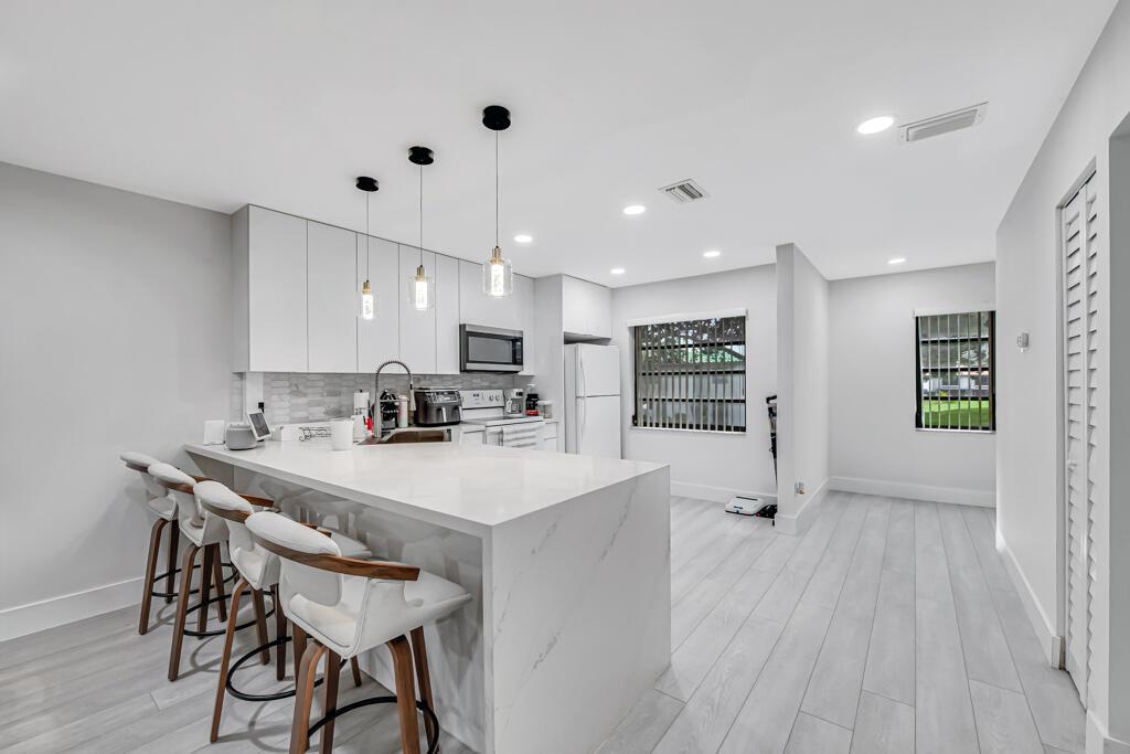 A modern kitchen features a white marble waterfall island, bar seating, and light wood flooring — 21362 Juego Circle # D, Boca Raton FL 33433, BOCA RATON, FL