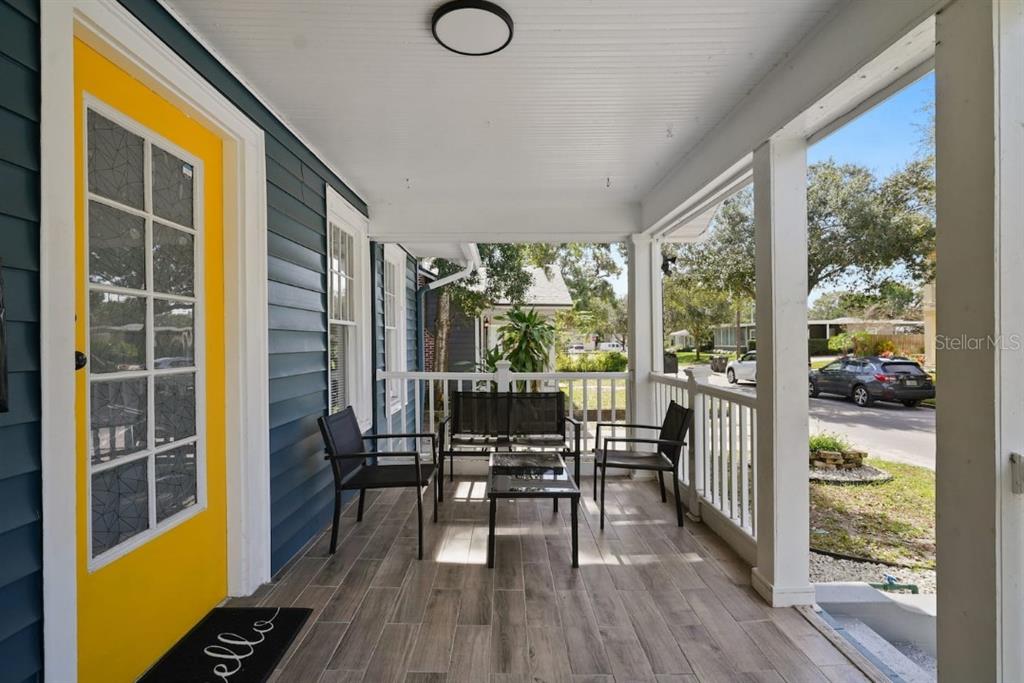 A covered front porch features blue siding, a bright yellow door, and wood-look tile flooring — 1829 HOLLENBECK DRIVE, ORLANDO, FL