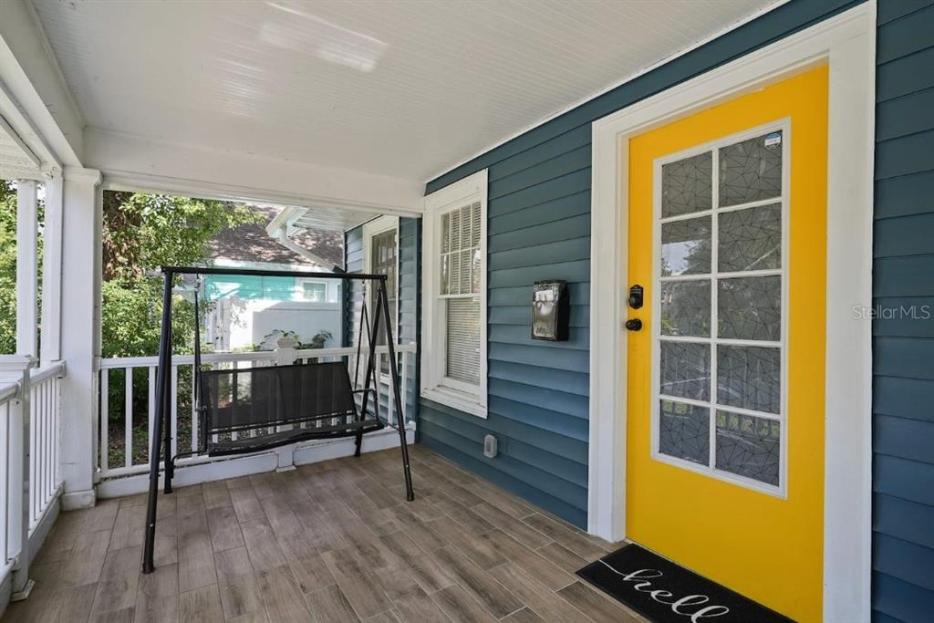 A covered porch features blue siding, a bright yellow door, and a black porch swing — 1829 HOLLENBECK DRIVE, ORLANDO, FL