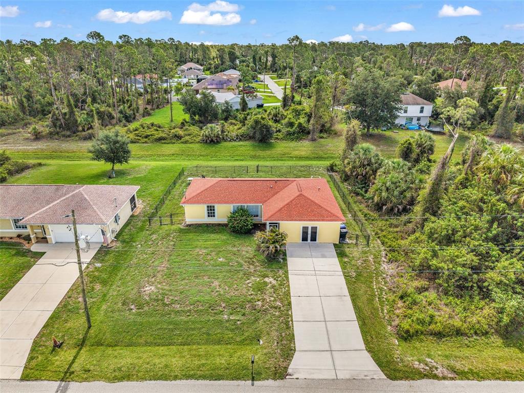 An aerial view shows a yellow single-story house with a red roof and concrete driveway — 1160 NUCELLI ROAD, NORTH PORT, FL
