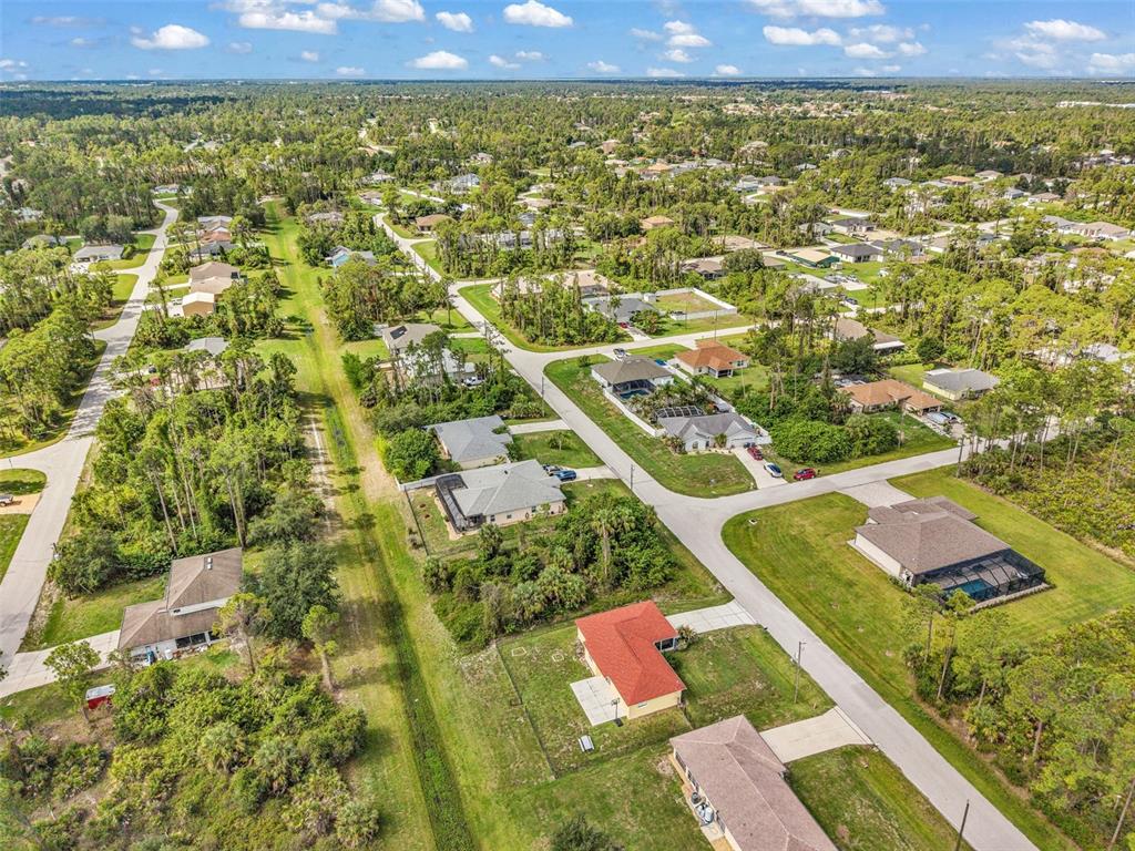 An aerial view shows a suburban neighborhood with single-family homes, paved roads, and wooded areas — 1160 NUCELLI ROAD, NORTH PORT, FL