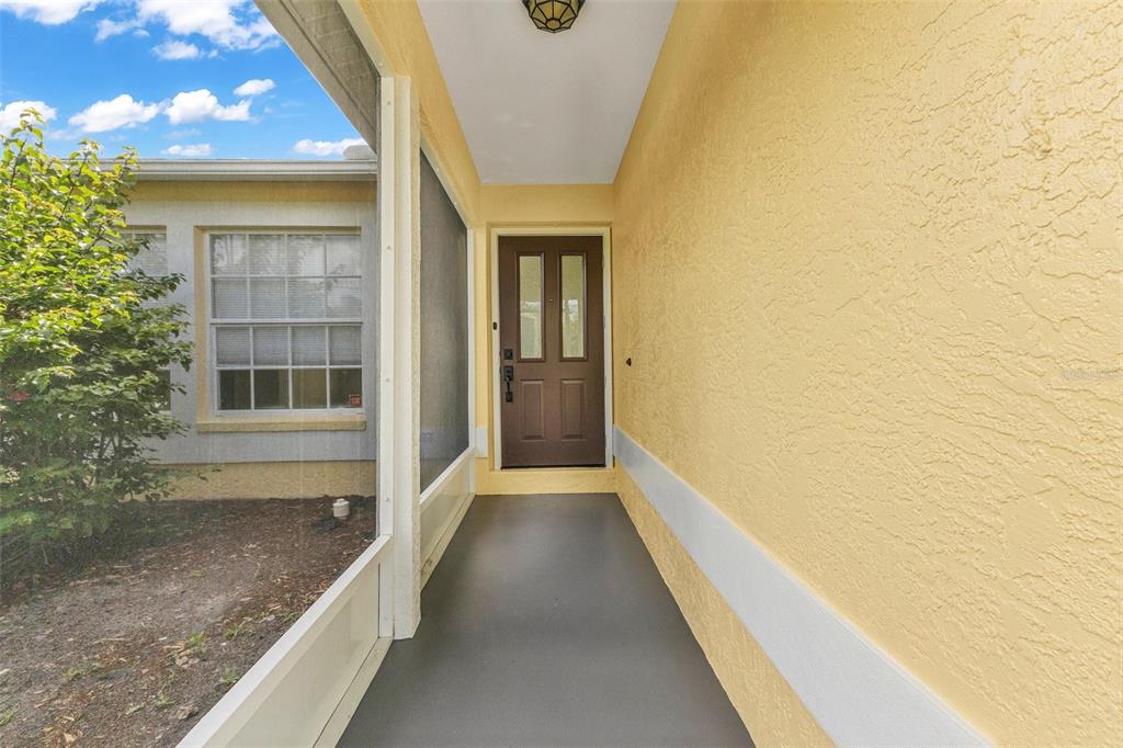 A covered entryway features a brown front door, yellow stucco walls, and a gray floor — 1160 NUCELLI ROAD, NORTH PORT, FL
