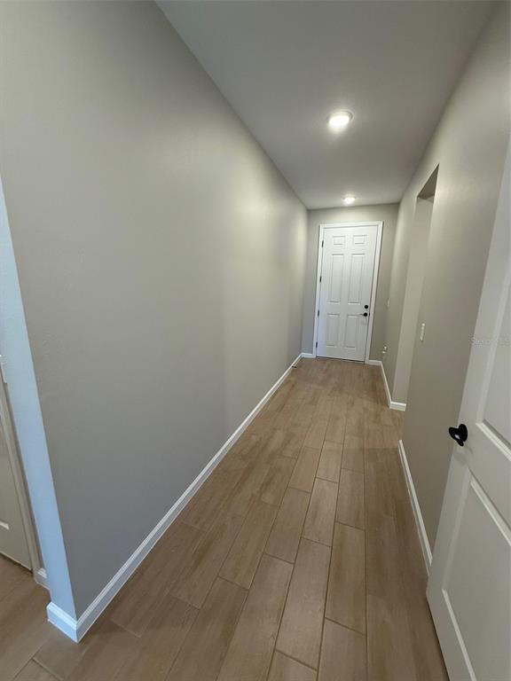 A hallway with light-colored walls and wood-look tile flooring leads to a white door — 10073 SPRING LAKE DRIVE, CLERMONT, FL