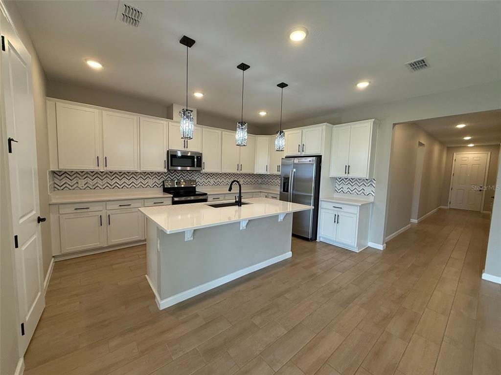 A modern kitchen features white cabinets, a central island, stainless steel appliances, and wood flooring — 10073 SPRING LAKE DRIVE, CLERMONT, FL