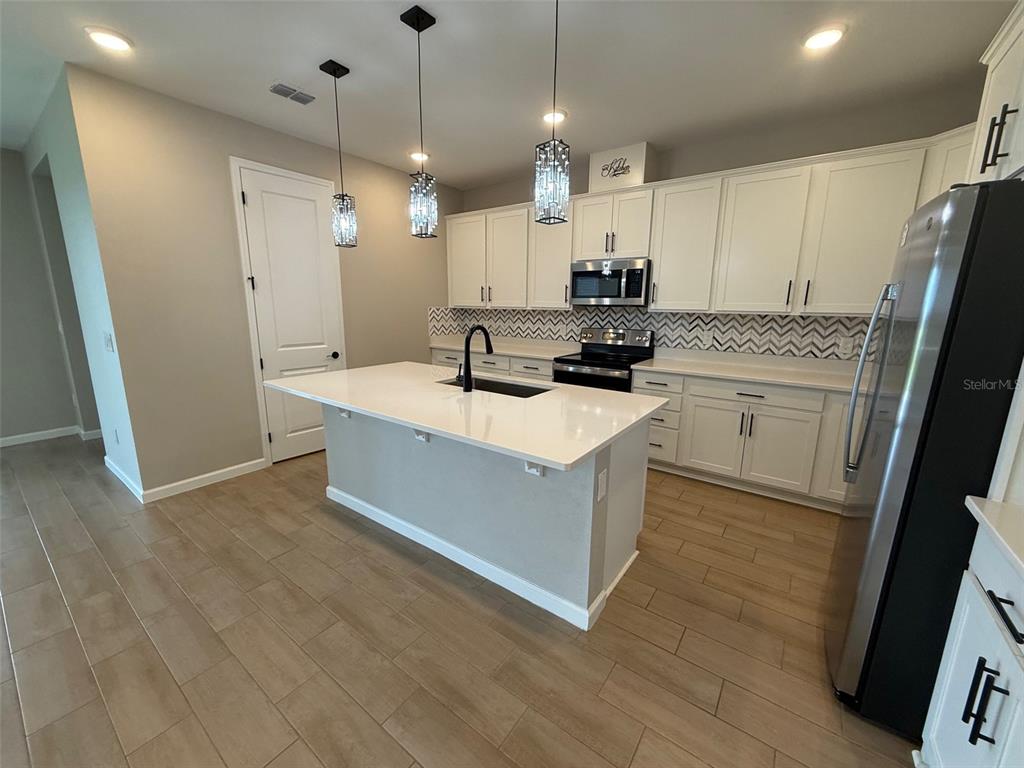 A kitchen features white cabinets, a central island with a sink, and wood-look tile flooring — 10073 SPRING LAKE DRIVE, CLERMONT, FL