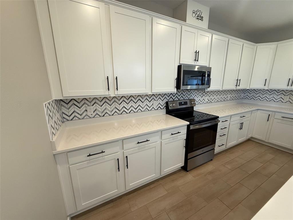 A kitchen featuring white cabinets, a chevron-patterned backsplash, stainless steel appliances, and light countertops — 10073 SPRING LAKE DRIVE, CLERMONT, FL