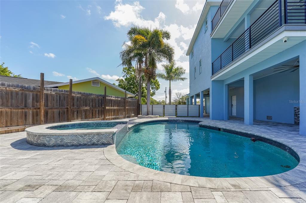 A backyard features a swimming pool with an attached spa and a blue multi-story house — 8717 DRIFTWOOD DRIVE, TAMPA, FL