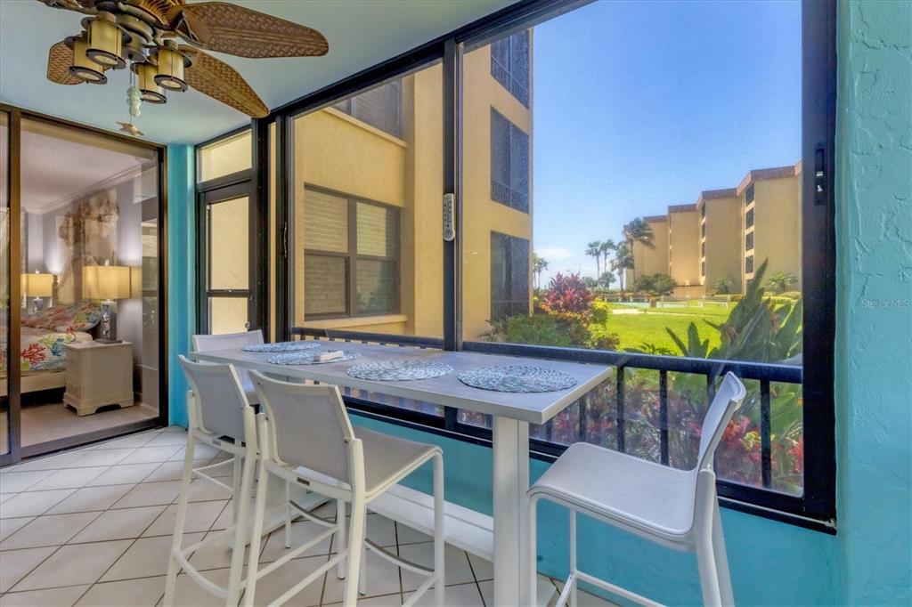 A sunroom with a high-top table, white chairs, tile flooring, and views of apartment buildings — 8776 MIDNIGHT PASS ROAD UNIT C107, SARASOTA, FL
